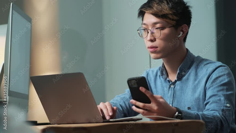 The confident Asian man recording something from phone to laptop while sitting in the light office