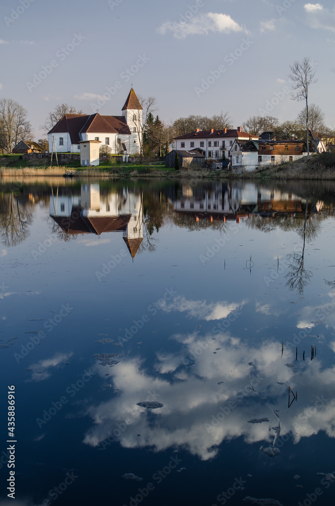 Alsunga catholic church and reflection in lake, Latvia. 