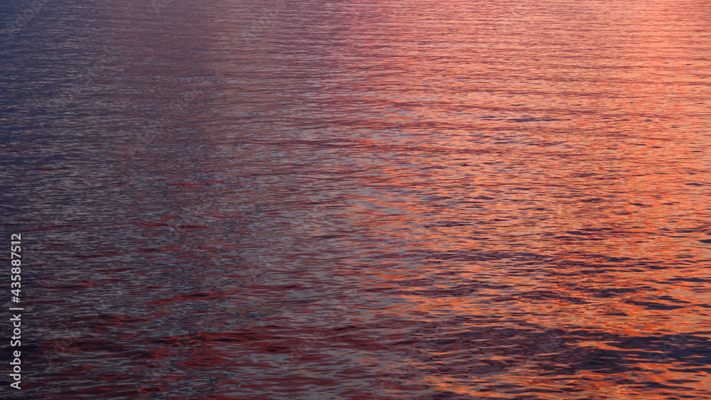 A three colored orange, pink and dark blue water surface with ripples and sunny reflections in a middle of the sea. Sunset or sunrise water reflection
