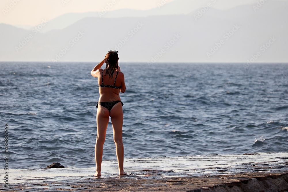 Beach vacation, tanned slim girl in bikini taking pictures on smartphone of mountain coast. Summer holidays on the sea