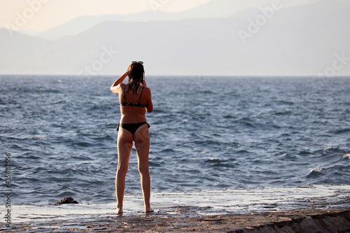 Beach vacation, tanned slim girl in bikini taking pictures on smartphone of mountain coast. Summer holidays on the sea