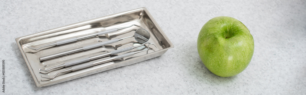 high angle view of metal dental tools in tray and green apple on medical table, banner. high angle view of metal dental tools in tray and green apple on medical table, banner.