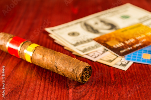 Cuban cigar and payment cards on a several dollar on the table. Close up view