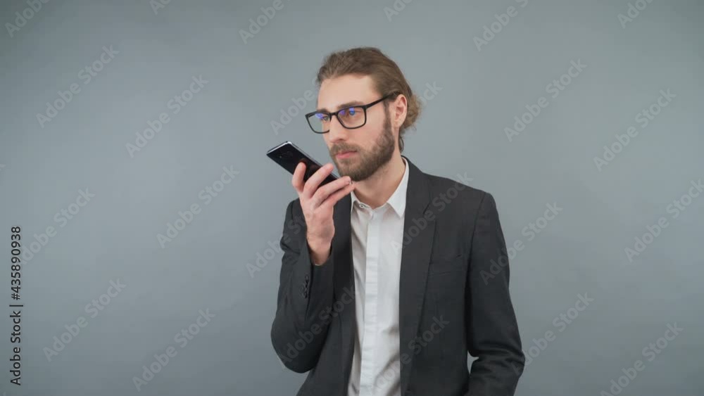 Business fashion modern businessman in a business suit and a wearing glasses writes a voice message. Man isolated on gray background. 4K Business fashion modern businessman in a business suit and a wearing glasses writes a voice message. Man isolated on gray background. 4K