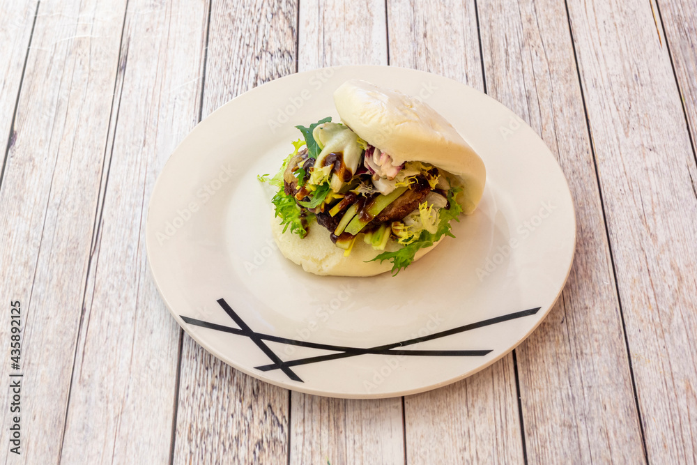 White plate with Asian duck loin bao bread with green sprout salad White plate with Asian duck loin bao bread with green sprout salad