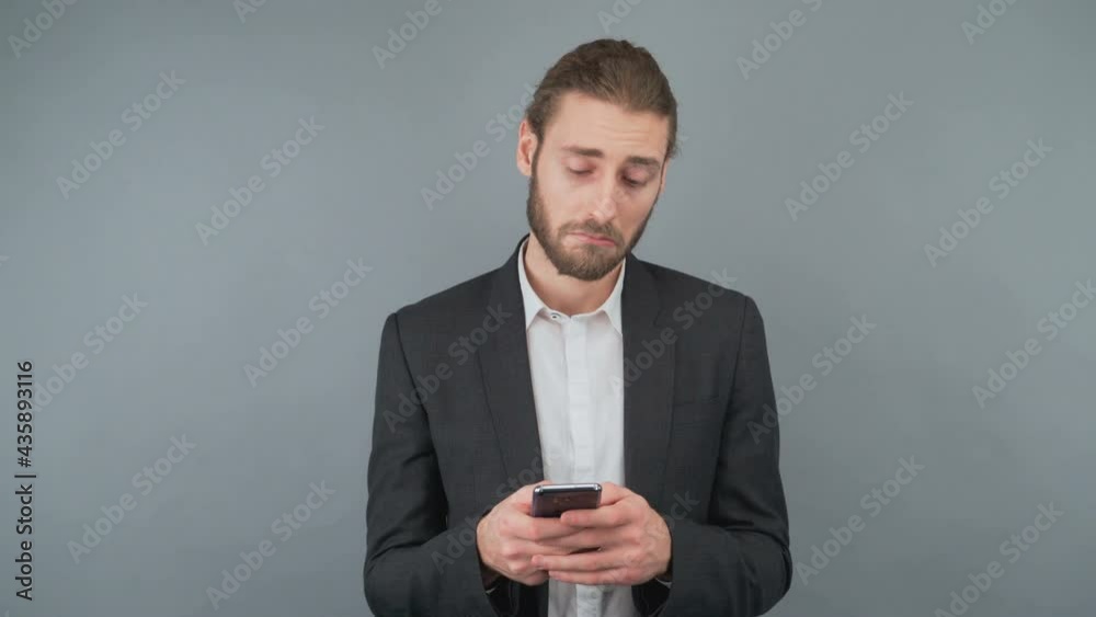 Portrait of a man with a smartphone on a gray background isolated. A man reads news and finds a good offer. 4K Portrait of a man with a smartphone on a gray background isolated. A man reads news and finds a good offer. 4K