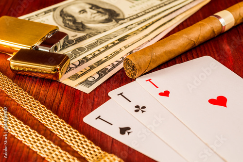 Cuban cigar and golden chain with playing cards and money on the table mahogany. Focus on the cuban cigar, identification cards ace Russian letter