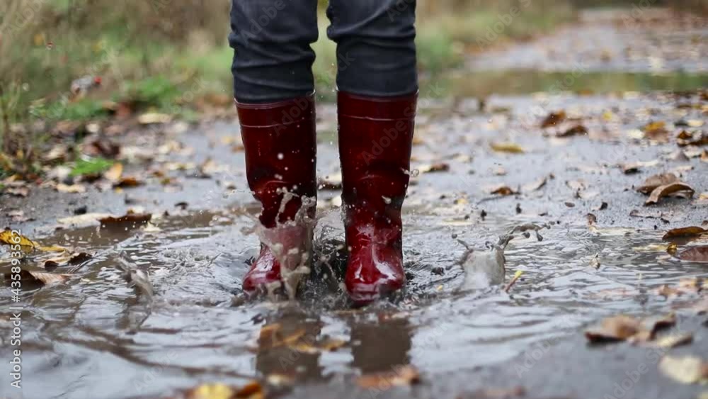 Closeup of woman in red rubber boots jumping in an autumn muddy puddle after rain Closeup of woman in red rubber boots jumping in an autumn muddy puddle after rain
