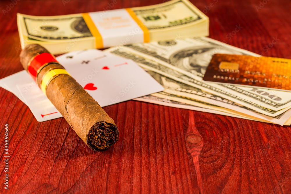 Cuban cigar with playing cards and money with payment card on the table mahogany. Focus on the cuban cigar, identification cards ace Russian letter