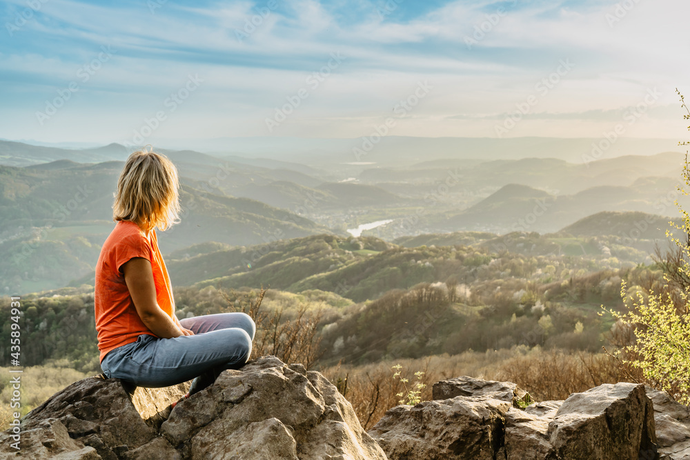 Female traveler with peaceful mind sitting on rock enjoying views of spring lush valley at sunset.Hiking day active lifestyle.Wanderlust woman relaxing outdoors.Travel freedom meditation concept