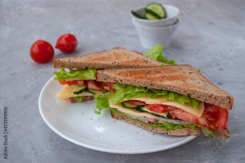 Delicious sandwich with fresh lettuce leaves, tomatoes, cucumbers and cheese on a grey table background.