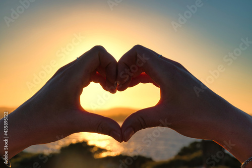 Woman Hands In Heart Symbol Shaped Lifestyle And Feelings Concept With Sunset at the beach