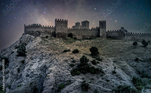 Medieval castle on a high rock at night. Stars on the sky. Medieval Genoese fortress in Crimea, Russia. Starry night in summer. Shrub growing on rocks. Ancient Fortress in Sudak.