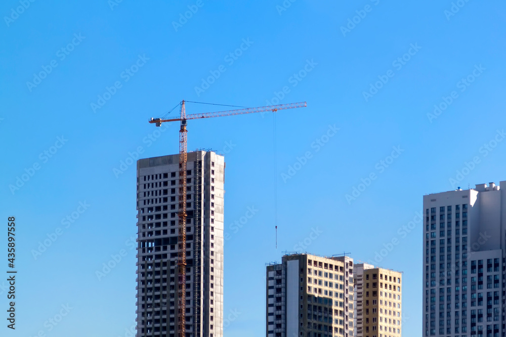 Construction cranes and unfinished residential buildings against clear blue sky. Housing construction, apartment block with scaffolding Construction cranes and unfinished residential buildings against clear blue sky. Housing construction, apartment block with scaffolding
