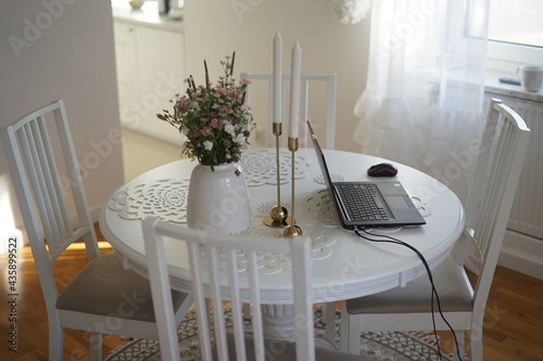 Home office. Laptop standing on the white round table. Beautifull bouquet of flowers and candles.