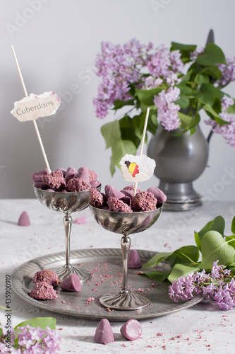 Belgian sweets cuberdon and pralines in silver glasses, spring still life with lilac flowers and flags photo