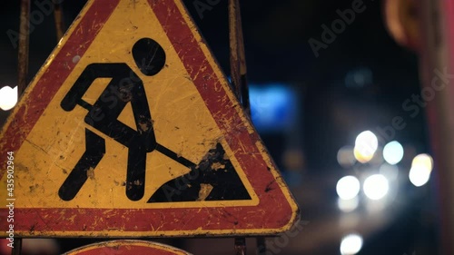 Close-up of a road sign warning drivers about road works. Grunge road traffic sign. Signal lights flash in the background.
