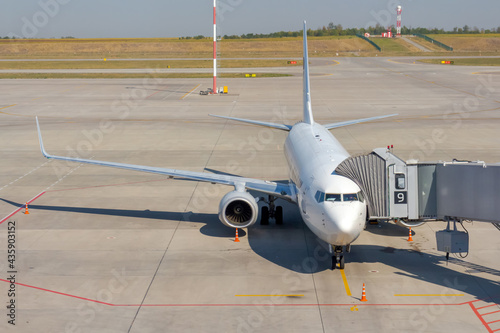Fotografia White commercial airplane docked on apron outside airport terminal with passenger boarding bridge