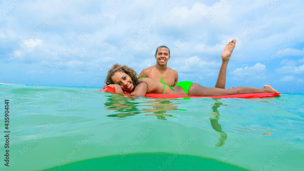 Couple at the beach playing, in the water with a float, interracial, black