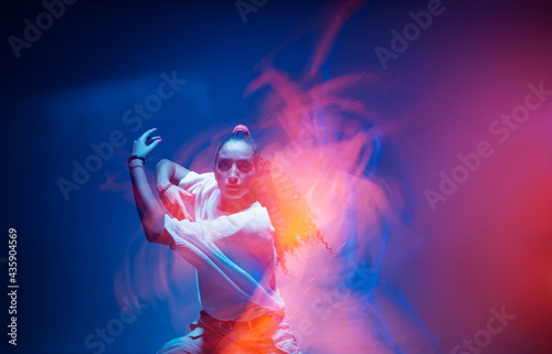 Dancing mixed race girl cool moving in colourful neon studio light. Long exposure. Fiery expressive contemporary dance