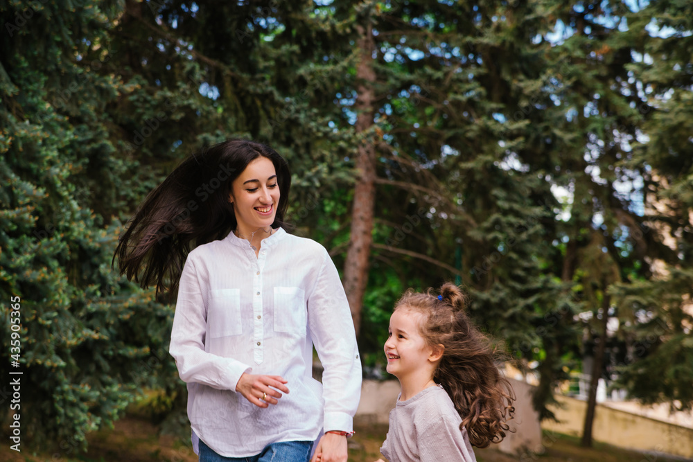 A little girl and her mother run along the sidewalk in the park. Active play in nature.