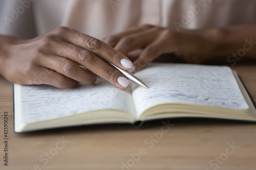 Close up young african american woman holding pen in hands, reading notes in copybook, repeating educational information preparing for exam. Focused mixed business lady managing assignments in planner