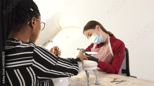 Nail master in mask doing manicure to an African American woman photo