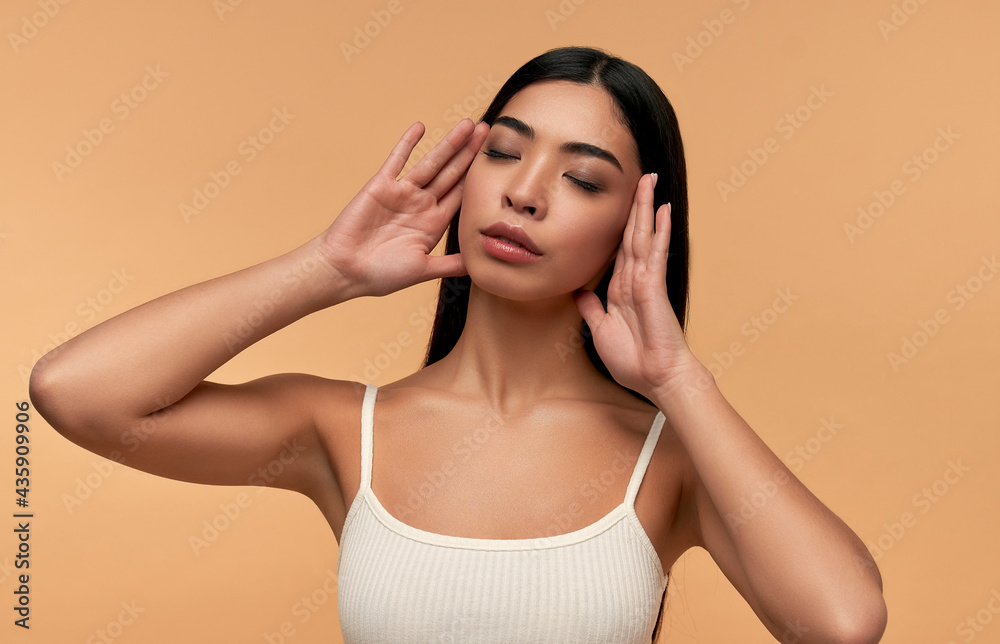 Young Asian woman with clean healthy glowing skin in white top isolated on beige background. Facial skin care concept, spa, cosmetology, plastic surgery. Young Asian woman with clean healthy glowing skin in white top isolated on beige background. Facial skin care concept, spa, cosmetology, plastic surgery.