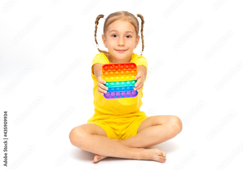 Young Little Girl Sitting On the white background and playing Poppit-New Fidget Toy, Popular With Kids, Helps Them To Concentrate. Child Playing With The Pop It Fidget Toy. Young Little Girl Sitting On the white background and playing Poppit-New Fidget Toy, Popular With Kids, Helps Them To Concentrate. Child Playing With The Pop It Fidget Toy.