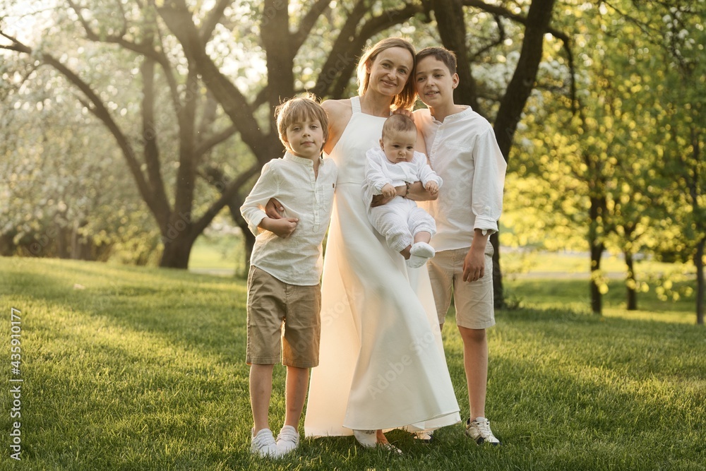 Mother and three children hugging. Happy family sitting outdoor: woman and two brother kids boys and cute little toddler boy Mother and three children hugging. Happy family sitting outdoor: woman and two brother kids boys and cute little toddler boy