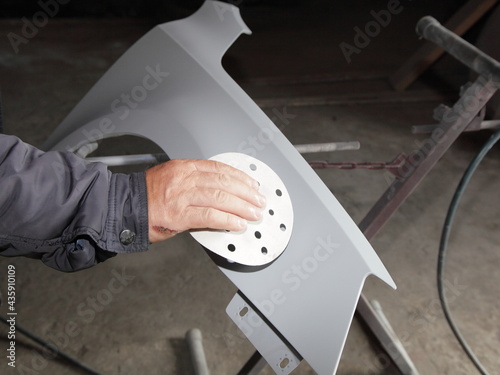 Manual dry sanding a car body part with abrasive paper before painting, vehicle body repair service