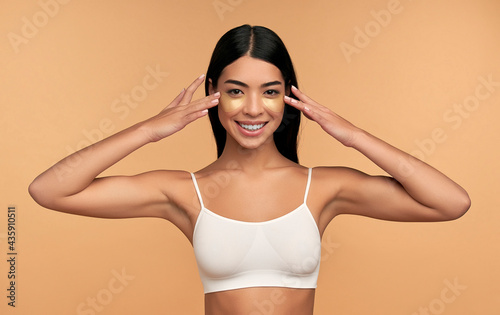 Fotografiet Young Asian woman in white lingerie and clean radiant skin with moisturizing patches under the eyes on a beige background