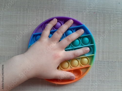 The toy is silicone anti-stress, multi-colored. The child's hand. The child is playing at the table. Light background.