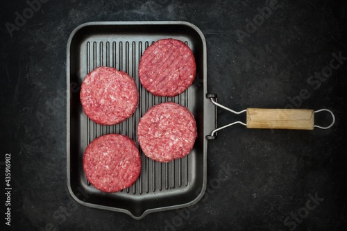 Raw Minced Homemade Grill Beef Burgers in Frying Pan, Top View. Griddle Grill Pap and Ground Beef Meat Patties for Grilling on Black Background, Overhead View. Raw Steak Burgers Cutlets On Grill Pan.
