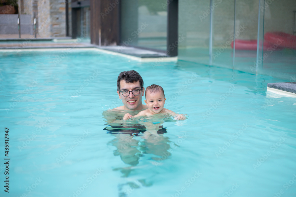 Dad in glasses for vision plays in the pool with his young daughter, summer fun in the water park. Blue water in the pool.