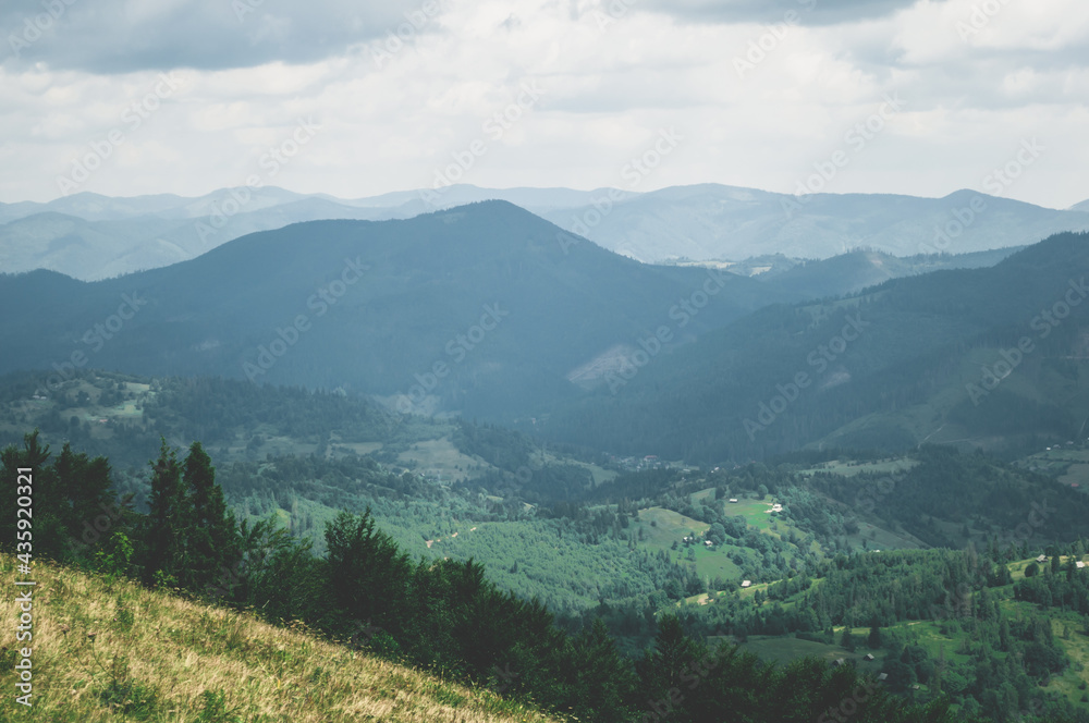 Obraz premium View from top mountain to wooded mountain landscape against background sky covered white-gray dense clouds.