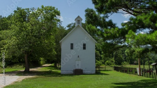 Timelapse of cloud movement over a mountain range, trees, and a white country church in a field of grass