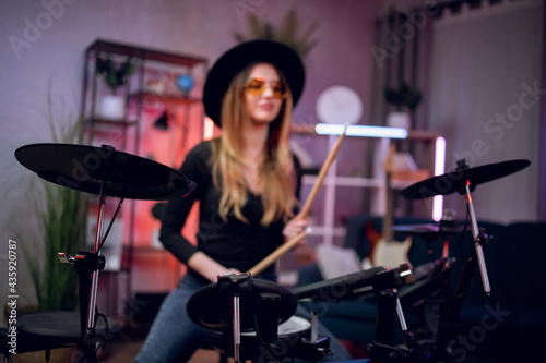 Inspired young lady in stylish outfit using electronic drums while recording sound at studio. Charming woman playing on music instrument at dark atmosphere,