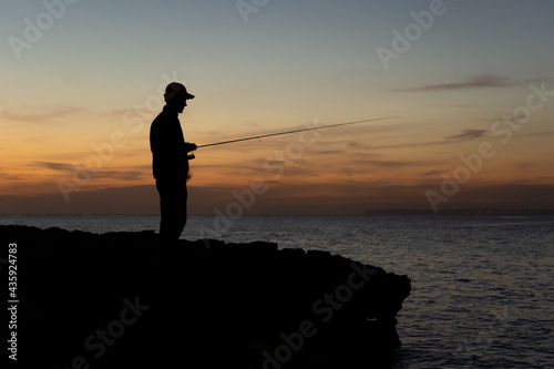 A fisherman with the rod at sunset against the light in Majorca, Spain