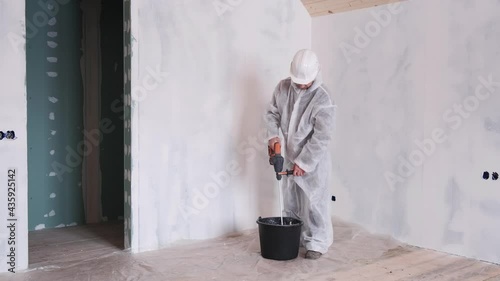 A full-length man in a protective suit and hard hat prepares cement for home repairs. Renovation of the house. A tool for building a house.