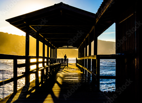 Silhouette of a man fishing at sunset in a beautiful deck with golden colors