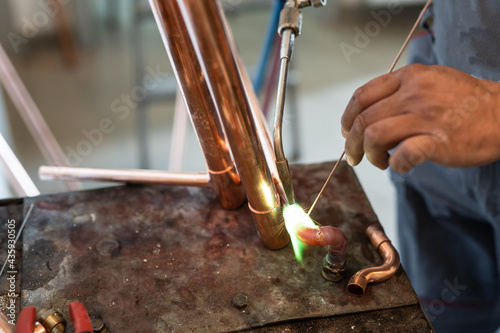 Close up on hands of unknown industrial worker plumber with central heating copper pipes welding using gas torch or blowtorch at work photo
