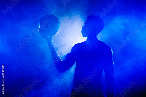 Basketball player holding a ball against blue fog background. African american man silhouette