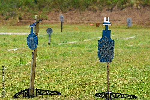 AR500 Steel gong and silhouette Shooting Targets on stands sitting on a grass field at a shooting range.