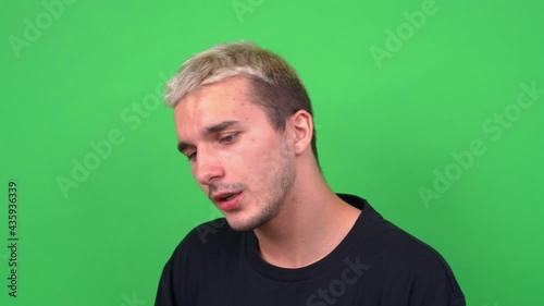 Handsome guy with dyed blond hair in black t-shirt posing for camera on chromakey closeup. Young guy with troubled teenage facial skin sensually recites poetry or sing. photo