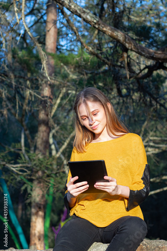 Mujer joven leyendo en una tableta y bosque de fondo