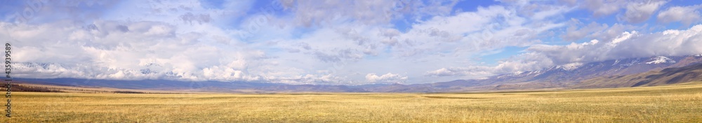 Kurai steppe in the Altai Mountains. Panorama of a wide spring plain surrounded by mountains under a cloudy sky. Pure Nature of Siberia, Russia