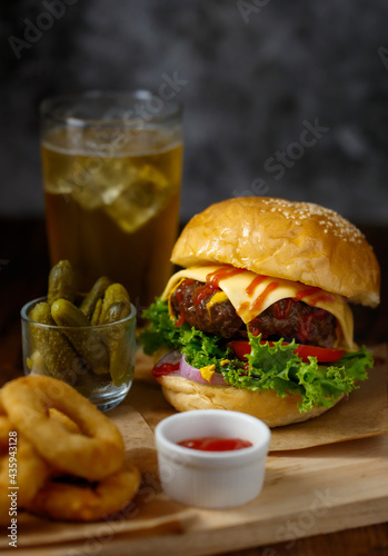 Selective focus on hamburgers with beef burgers, fried onions, spinach, ketchup, pepper, mustard sauce and cheese served fresh onions on a wooden board with soft drink in loft background