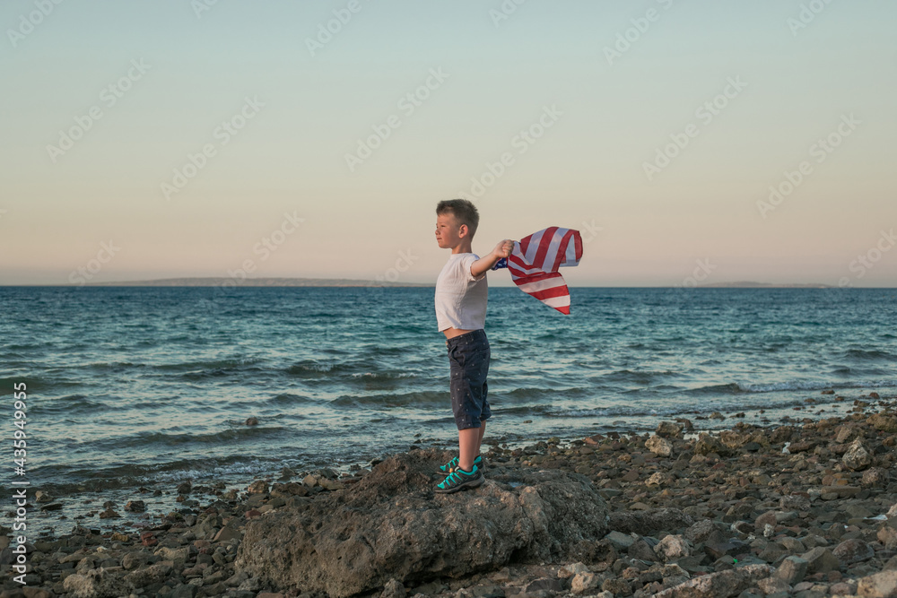 Little boy lets the american flag fly in his hands on the wind at the Sea. Patriotic family celebrates usa independence day on 4th of July.