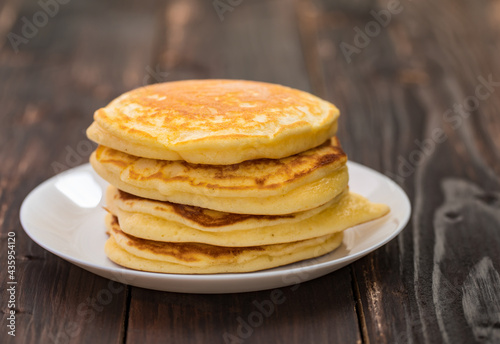 Stack of delicious pancakes in white plate on brown wooden background. It is a homemade breakfast Thick, soft, scented with butter.
